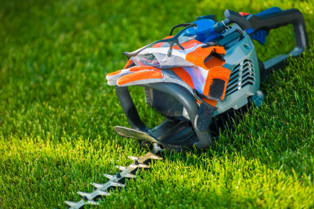 gas powered hedging tool in grass with gloves and safety glasses